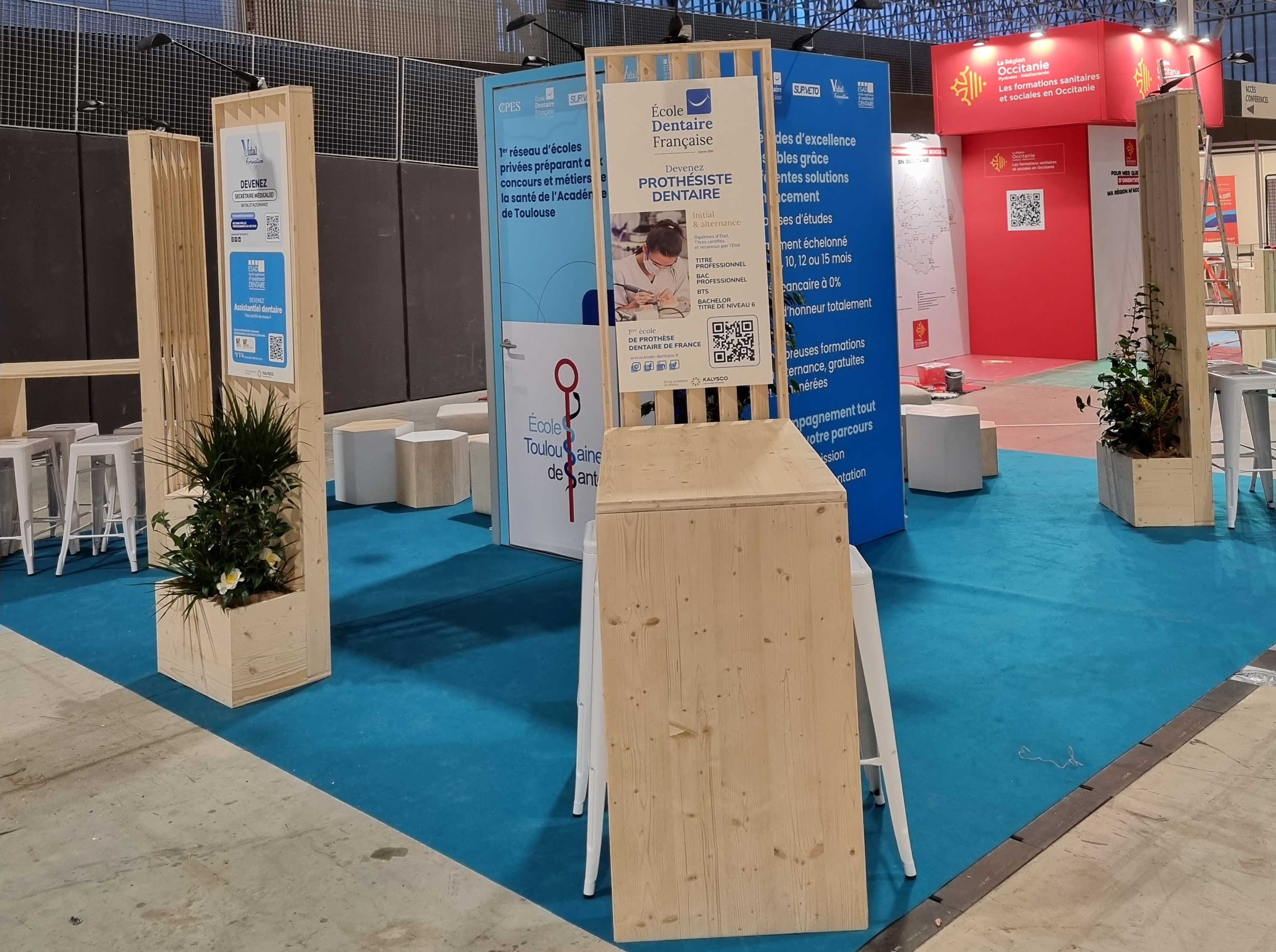 Stand de kalysco avec un sol moquette bleu et des claustras et desks en bois