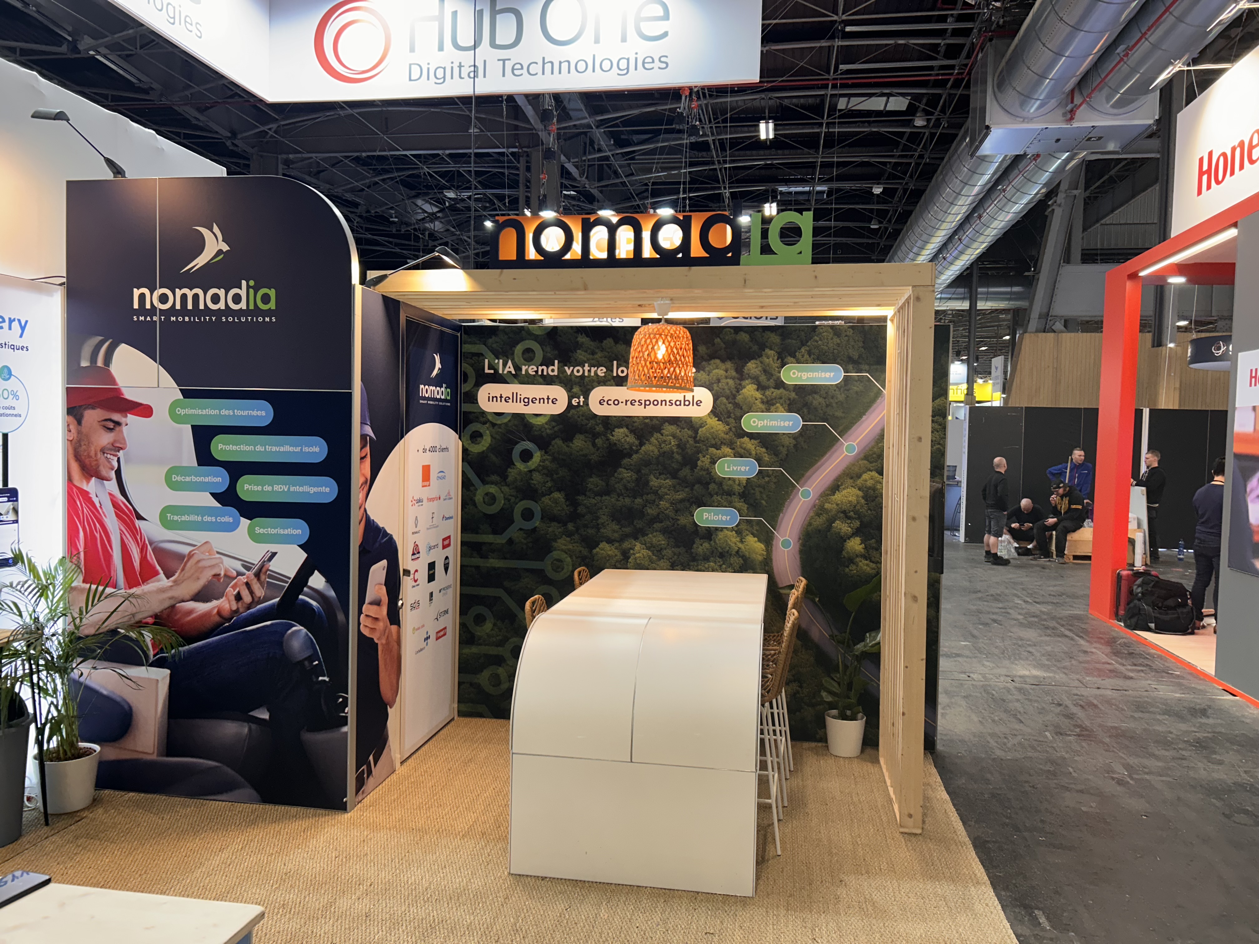 Stand de Nomadia au SITL 2025 avec cadre arrondi et desk arrondi, lettres en bois sur la claustra