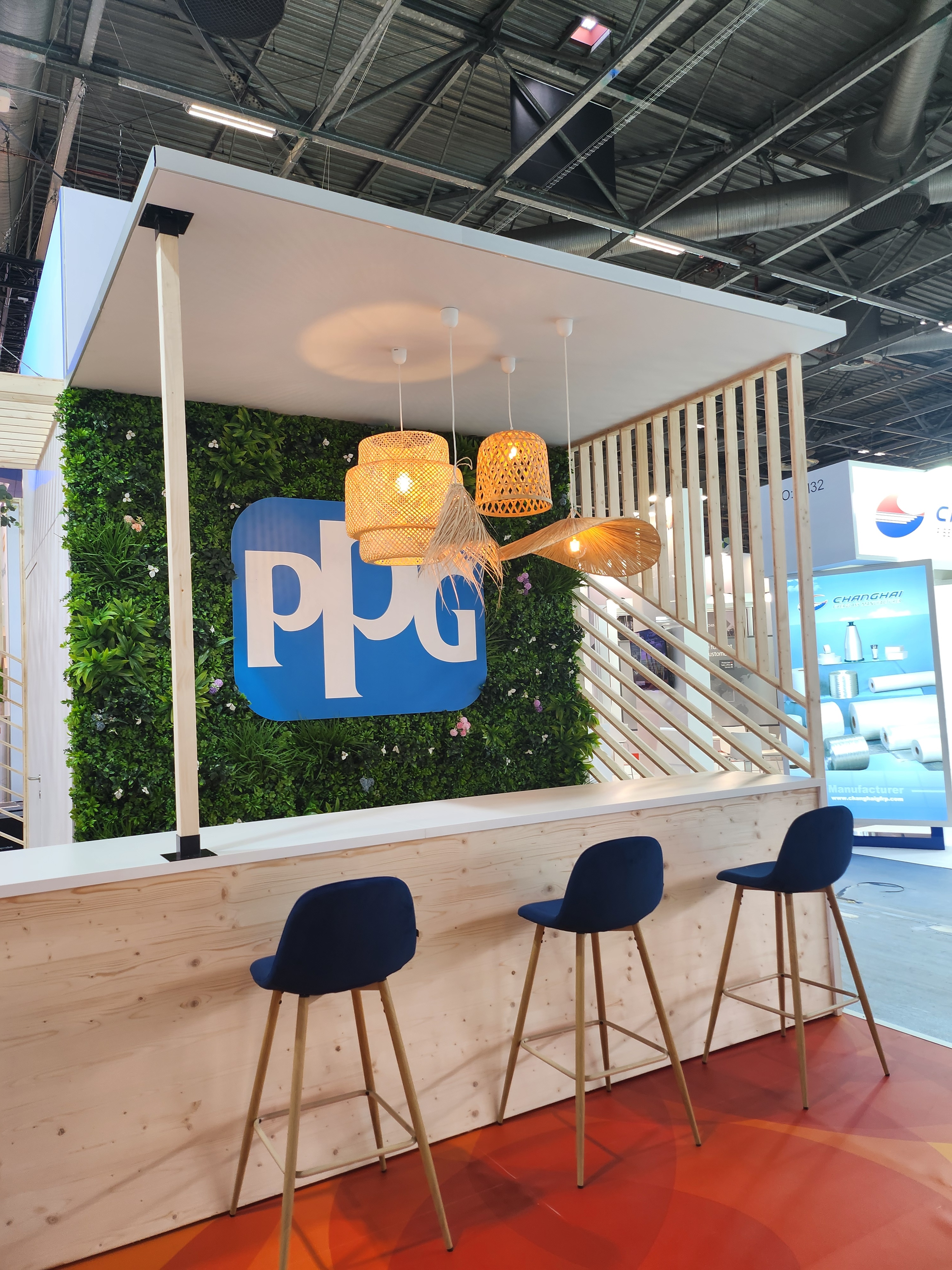 Bar d'accueil sur le stand de PPG au salon JEC World, tabourets hauts en velours bleu et bar en bois